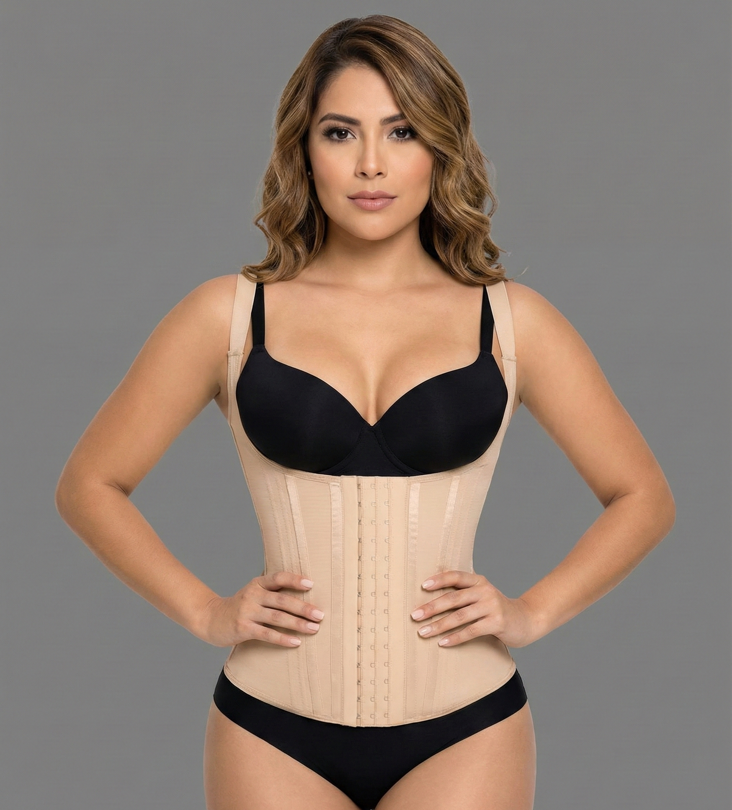 Woman wearing a black bra and beige waist trainer against a gray background