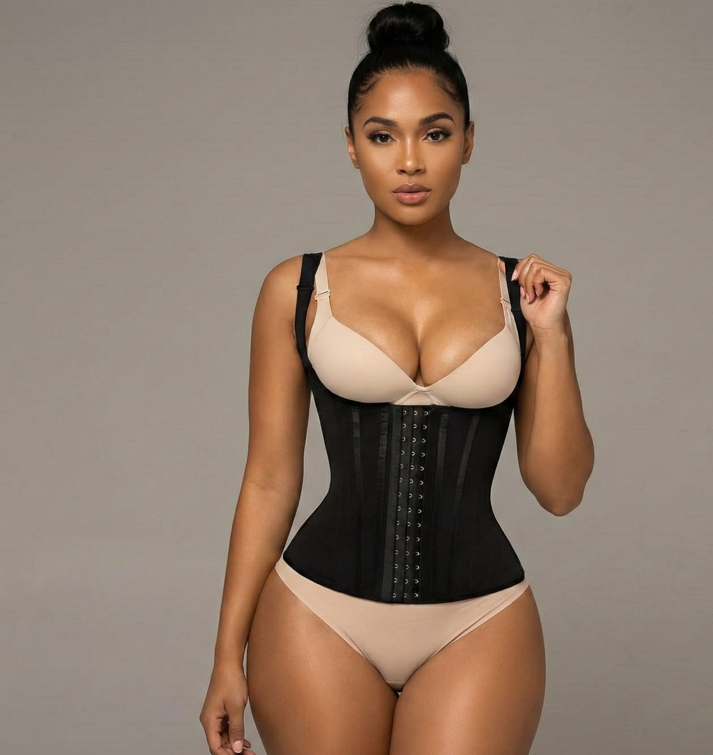 Woman wearing a black waist trainer and beige bra and panties on a gray background