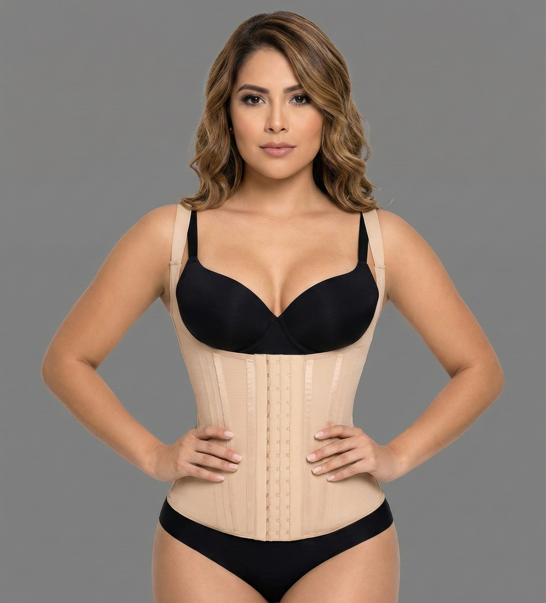 Woman wearing a black bra and beige waist trainer against a gray background